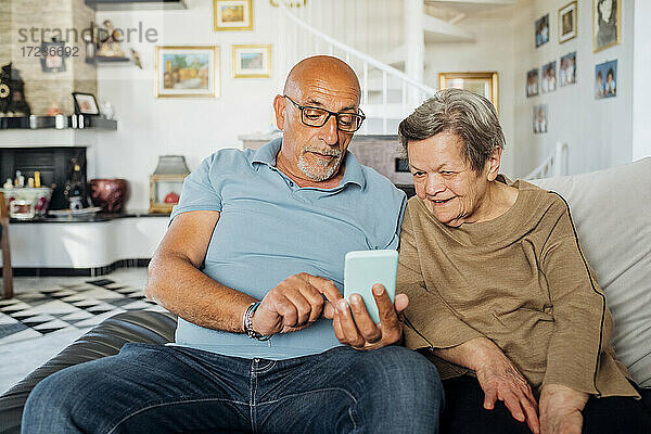 Älterer Mann benutzt sein Smartphone  während er mit seiner Mutter auf dem Sofa im Wohnzimmer sitzt