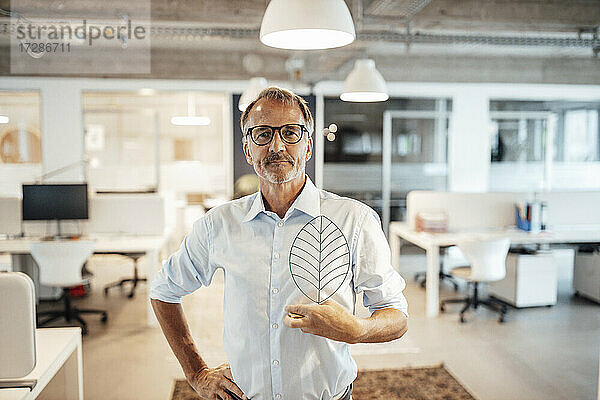 Selbstbewusster älterer Geschäftsmann  der ein Blattmodell mit der Hand auf der Hüfte im Büro hält