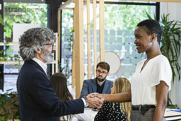Lächelnde männliche und weibliche Unternehmer schütteln sich die Hände mit Kollegen bei einer Besprechung im Büro