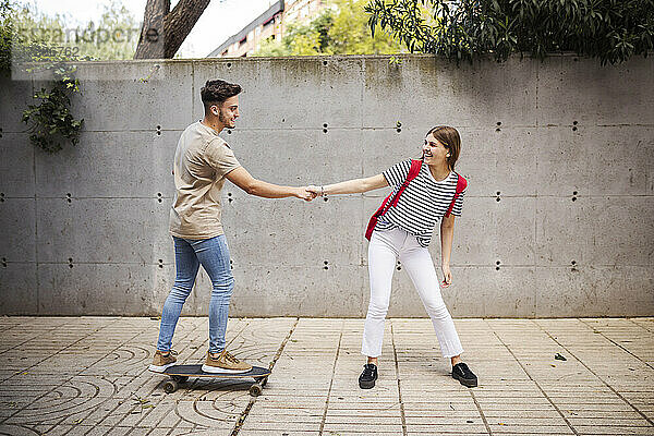 Freund hält die Hand seiner Freundin beim Skateboardfahren auf dem Gehweg