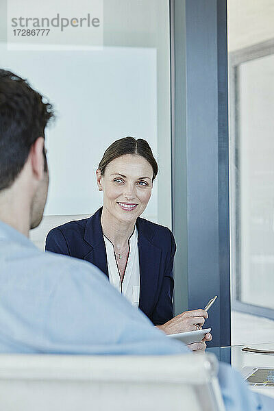 Lächelnde Immobilienmaklerin  die einen männlichen Kunden ansieht  während sie ein Gespräch führt