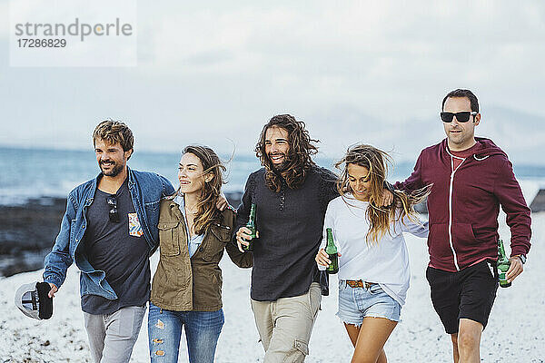 Männer und Frauen mit Bierflaschen gehen zusammen am Strand spazieren