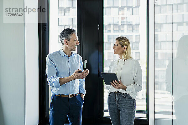 Geschäftsfrau  die ein digitales Tablet hält und einen männlichen Kollegen betrachtet  der eine Strategie im Büro diskutiert