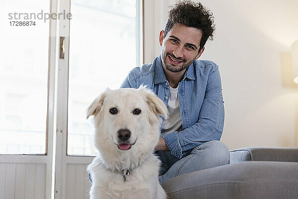 Lächelnde Mitte erwachsenen Mann mit niedlichen Hund im Wohnzimmer zu Hause