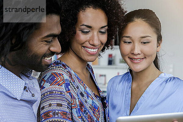 Lächelnde männliche und weibliche Fachkräfte  die auf ein digitales Tablet schauen  während sie sich im Büro unterhalten