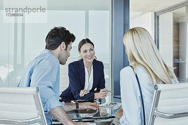 Lächelnde Verkäuferin im Gespräch mit einem Paar am Tisch sitzend