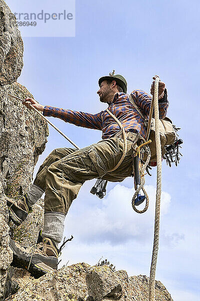 Männlicher Bergsteiger mit Sicherheitsgurt beim Bergsteigen an einem sonnigen Tag