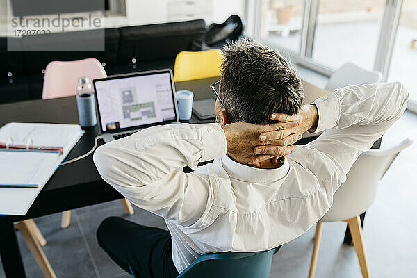 Entspannte männliche Design-Profi mit Händen hinter dem Kopf sitzen vor dem Laptop im Büro zu Hause