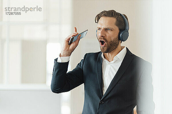 Geschäftsmann mit Smartphone hört Musik über Kopfhörer im Büro