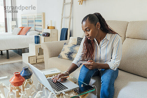 Mittlere erwachsene Frau  die einen Laptop benutzt  während sie mit einem Notizblock zu Hause sitzt