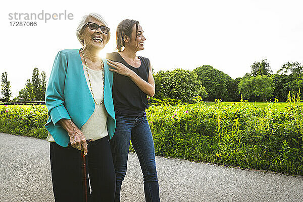 Glückliche ältere Frau  die mit einer Frau im mittleren Erwachsenenalter im Park spazieren geht