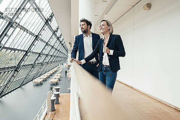 Lächelnde männliche und weibliche Unternehmer stehen an einem Geländer im Büro
