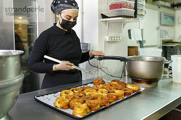 Bäckerin beim Frittieren von Krapfen in der Großküche einer Bäckerei