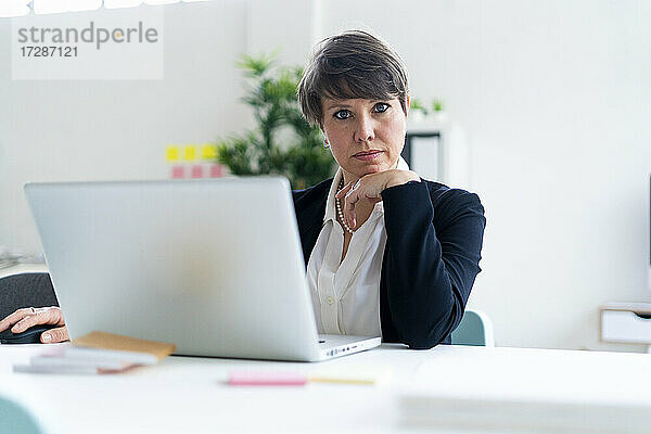Geschäftsfrau sitzend mit Hand am Kinn am Schreibtisch im Büro