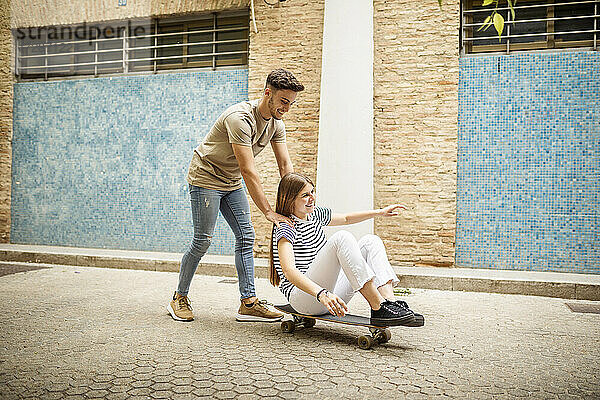 Fröhliches Paar spielt mit Skateboard auf dem Fußweg