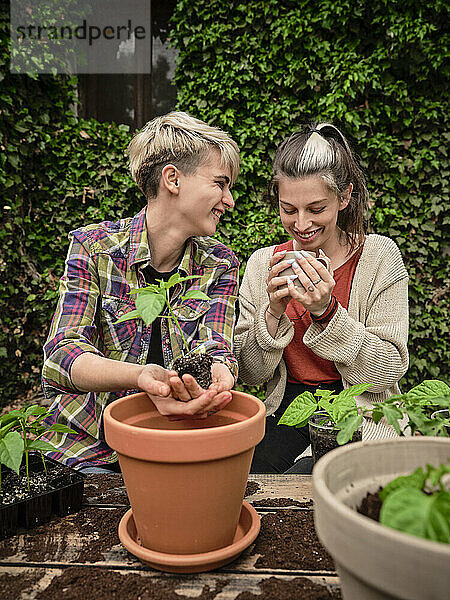 Lächelnde Frau sieht ihre Freundin an  die Kaffee trinkt  während sie im Garten pflanzt