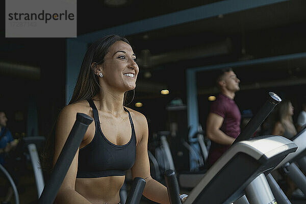 Lächelnde Sportlerin schaut weg  während sie auf dem Laufband im Fitnessstudio trainiert