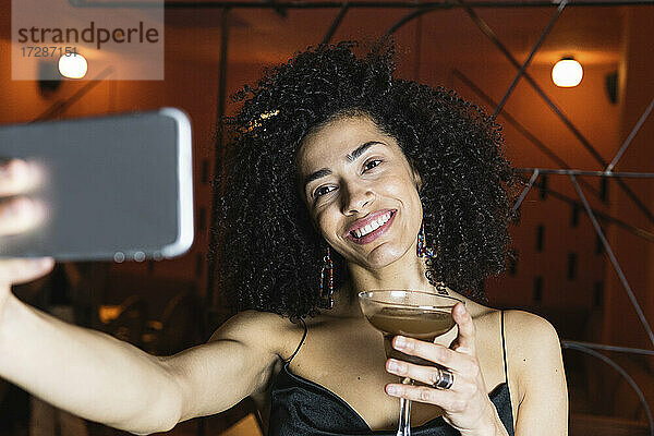 Junge Frau hält ein Getränk und macht ein Selfie mit ihrem Smartphone im Restaurant