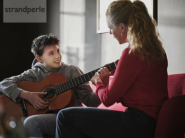Mutter hilft ihrem Sohn beim Gitarre spielen zu Hause