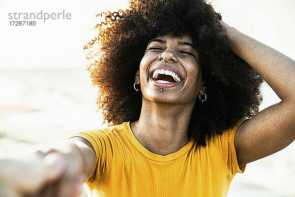 Afro-Frau lachend  während sie die Hand ihres Freundes am Strand bei Sonnenuntergang hält