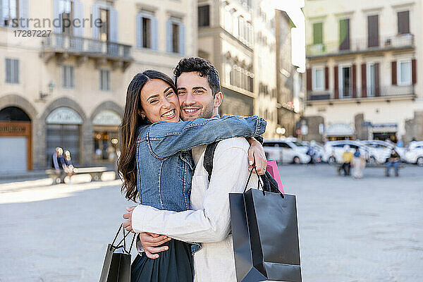 Lächelndes Touristenpaar  das Einkaufstüten hält und sich in der Stadt umarmt