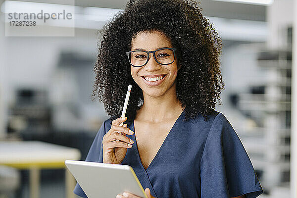 Lächelnde Unternehmerin mit digitalem Tablet und digitalisiertem Stift im Büro stehend