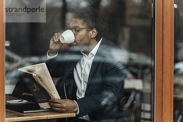 Geschäftsmann trinkt Kaffee und liest Zeitung in einem Café  gesehen durch Glas