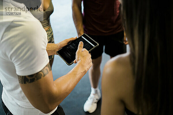 Mann mit digitalem Tablet im Gespräch mit männlichen und weiblichen Freunden im Fitnessstudio
