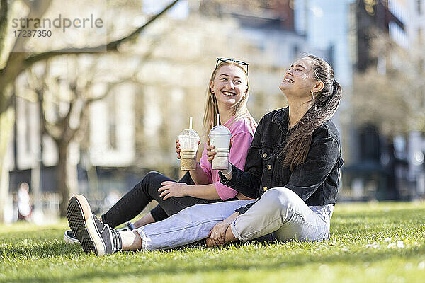 Fröhliche Freundinnen trinken einen Milchshake im öffentlichen Park