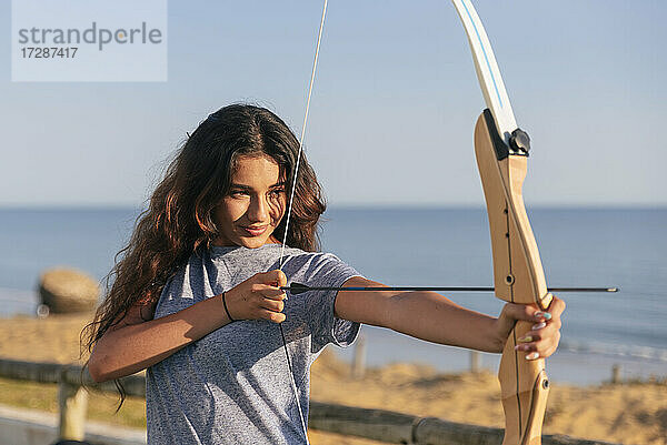 Lächelnde junge Frau  die an einem sonnigen Tag Bogenschießen übt