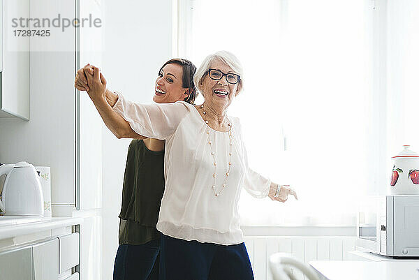 Glückliche ältere Frau tanzt mit Enkelin in der Küche zu Hause