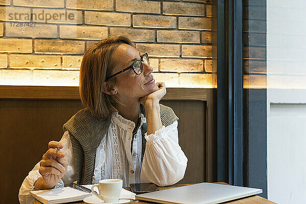 Frau mit Hand am Kinn träumt  während sie durch das Fenster eines Cafés schaut