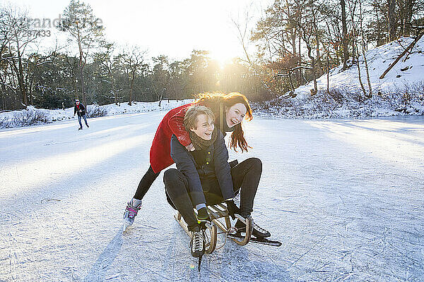 Fröhliches Paar beim Schlittenfahren und Schlittschuhlaufen auf einem zugefrorenen See