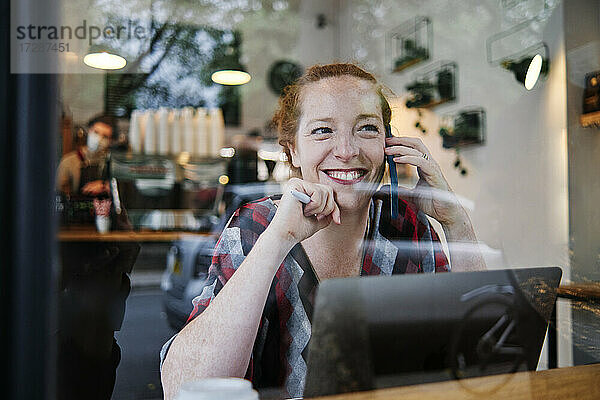 Lächelnde Frau  die wegschaut  während sie in einem Café mit ihrem Smartphone telefoniert