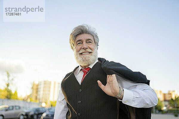 Lächelnder Geschäftsmann mit Anzugjacke auf der Schulter in der Stadt