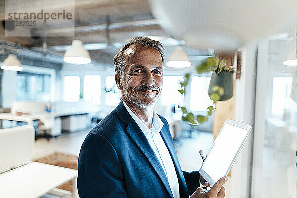 Lächelnder männlicher Unternehmer mit digitalem Tablet im Büro