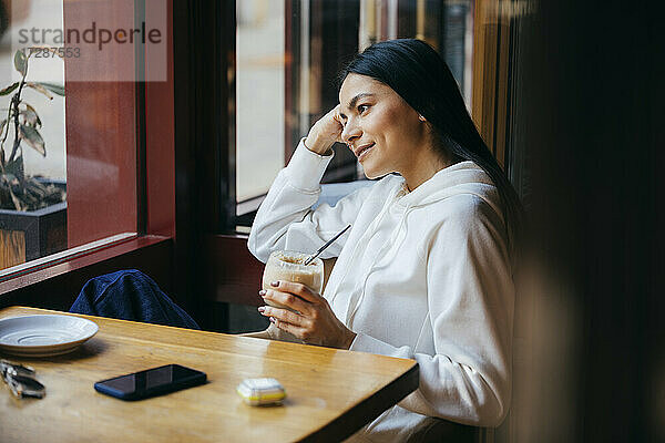 Lächelnde Frau schaut weg  während sie ein Getränk im Café hält