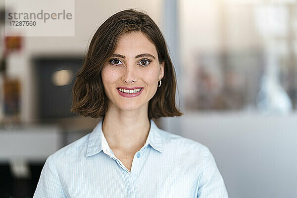 Schöne lächelnde junge weibliche Fachkraft mit braunen Haaren im Büro