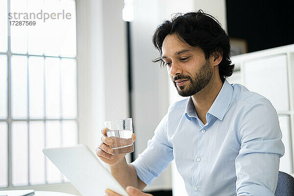 Geschäftsmann mit Trinkglas und digitalem Tablet im Büro