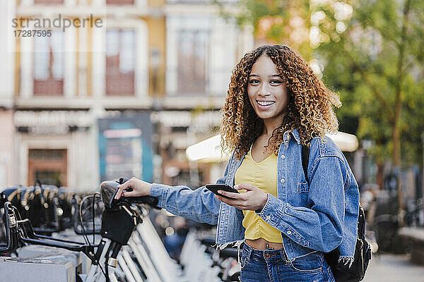 Lächelnde Frau mit Smartphone in der Nähe einer Fahrradabstellanlage