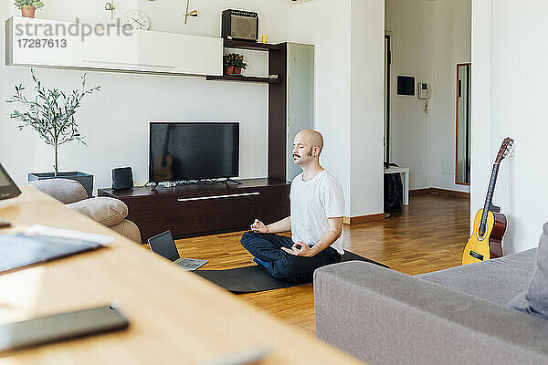 Junger Mann  der zu Hause über seinen Laptop online Yoga lernt