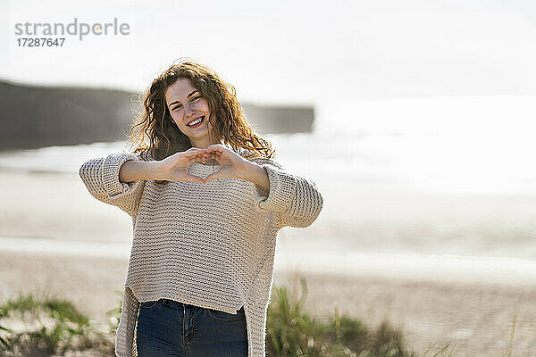 Lächelnde junge Frau mit Herzform am Strand