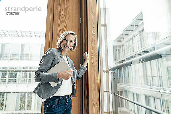 Geschäftsfrau mit digitalem Tablet am Bürofenster stehend