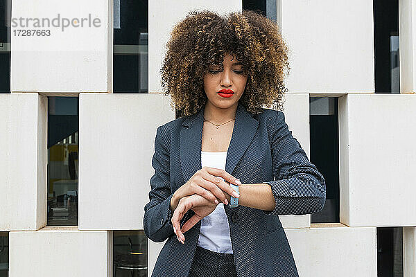 Attraktive Geschäftsfrau mit Armbanduhr prüft die Zeit vor einer modernen Wand