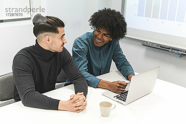Lächelnde männliche Fachkraft mit Laptop  die einen Kollegen im Büro ansieht