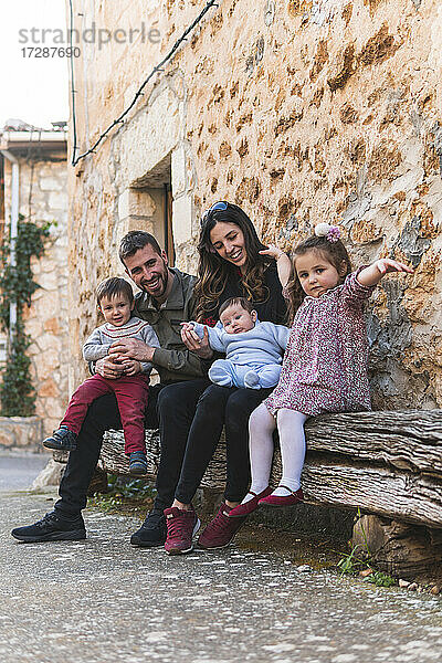 Glückliche Familie sitzt auf einer Bank mit einem Haus im Hintergrund