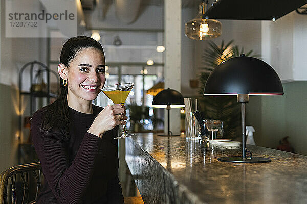 Lächelnde Frau hält ein Martini-Glas  während sie im Restaurant sitzt