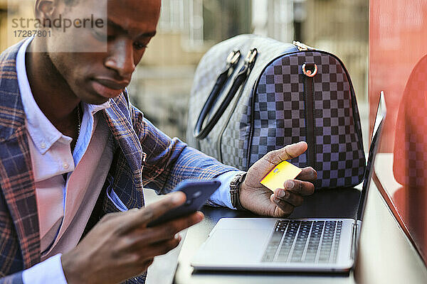 Geschäftsmann mit Kreditkarte und Mobiltelefon in einem Straßencafé