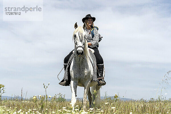 Junge Frau auf einem Pferd sitzend und wegschauend an einem sonnigen Tag