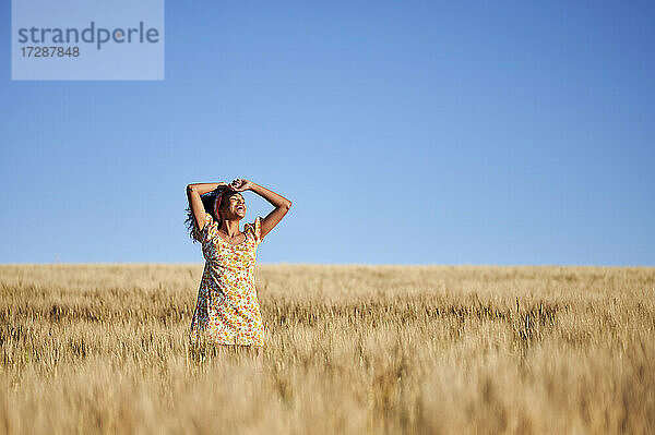 Fröhliche Frau steht in einem Weizenfeld vor blauem Himmel